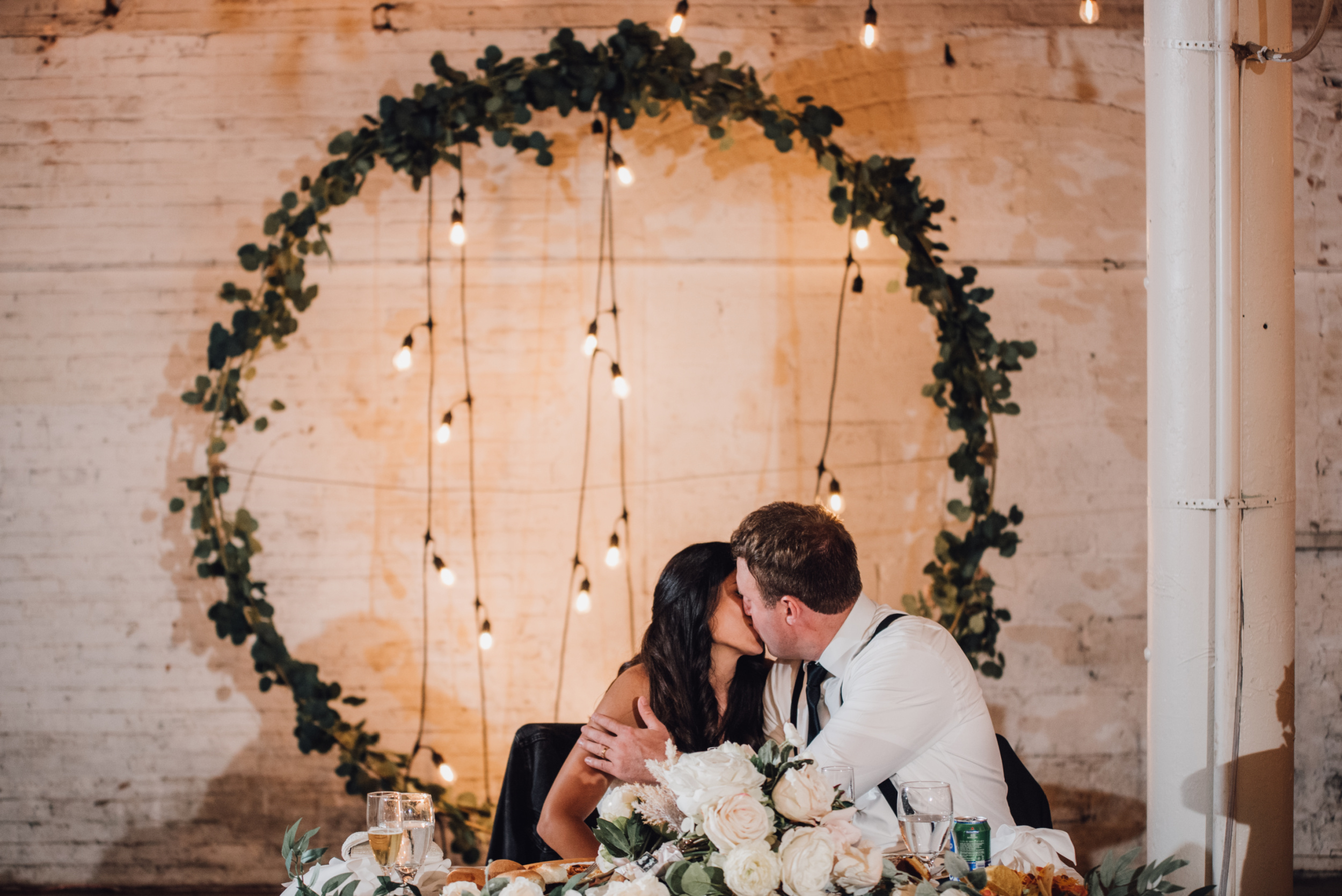 Bride and groom kissing at head table with greenery arch