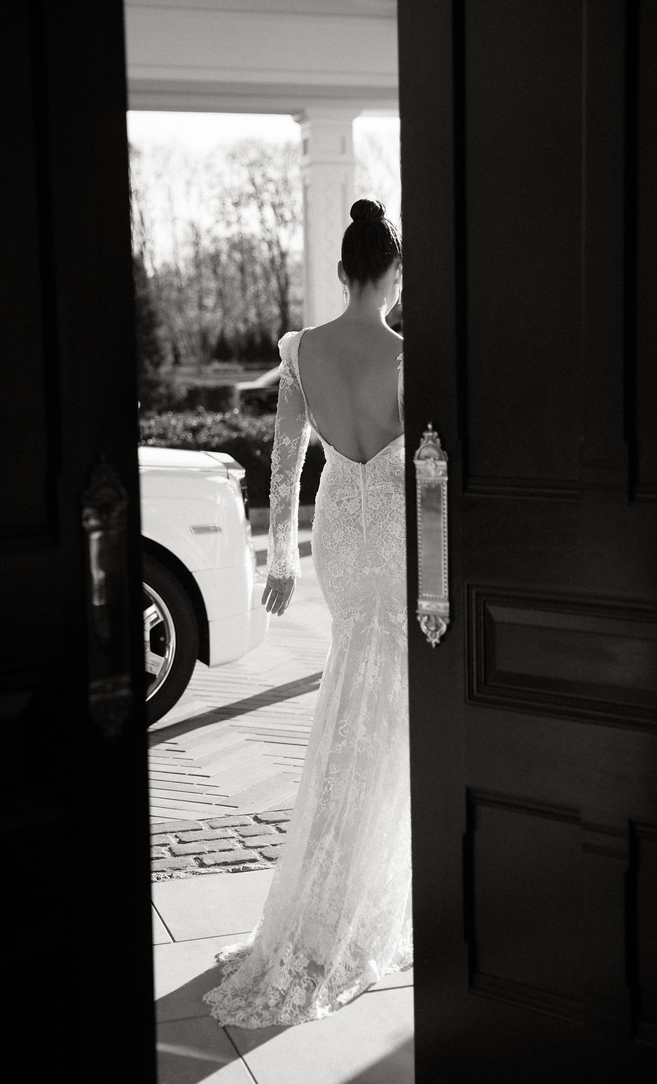 Bride in an open-back lace gown stepping through the open doors of the Shadowbrook estate
