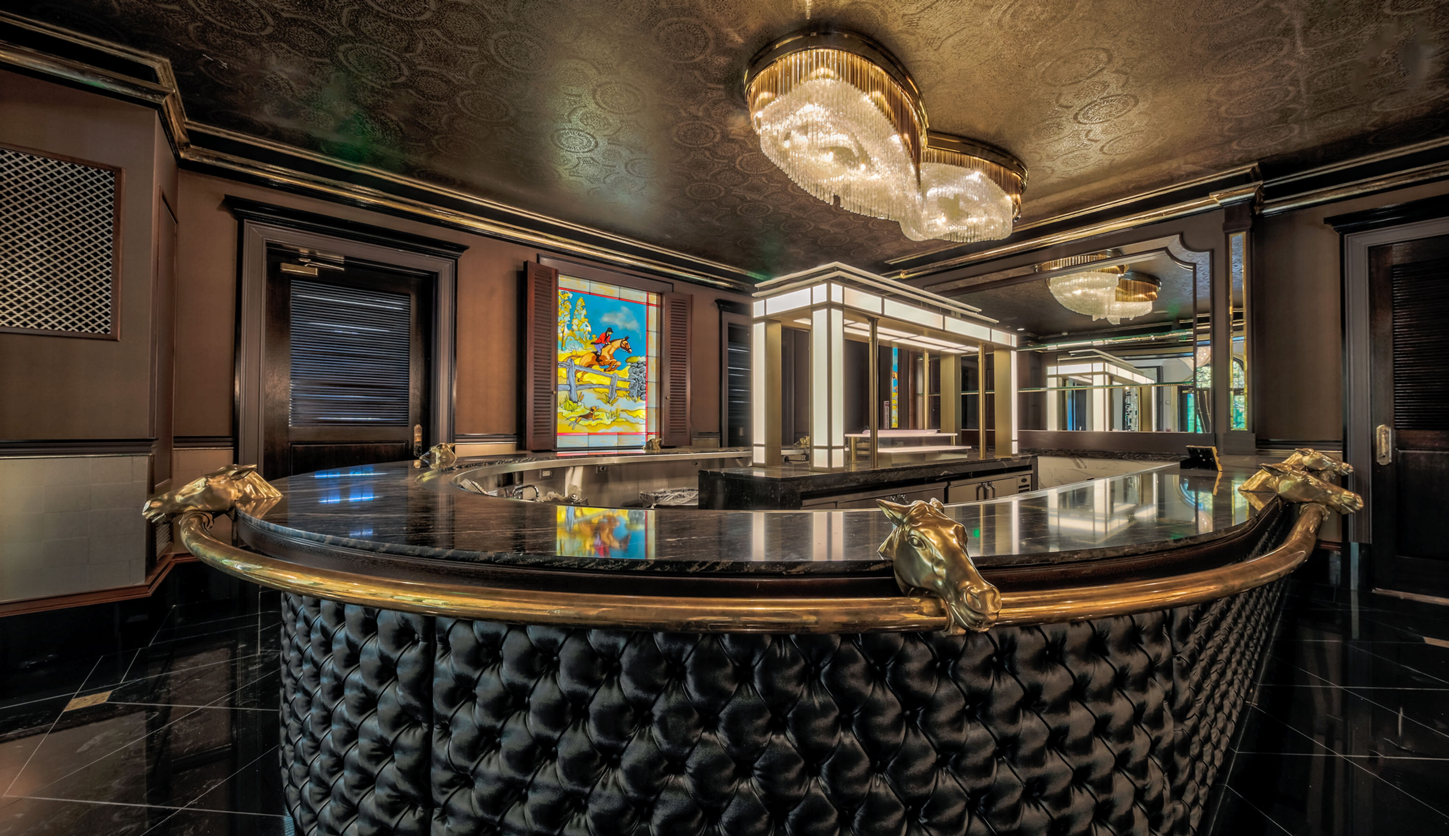 Curved upscale bar with black tufted leather, gold accents and a stained-glass window