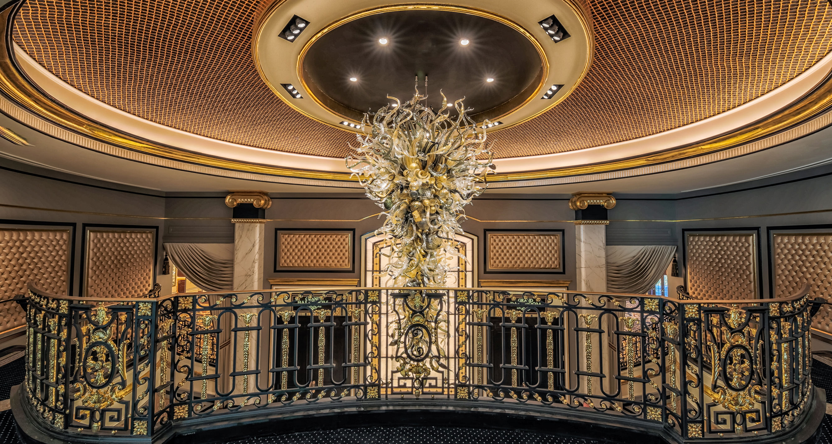 Balcony overlook with an elaborate glass chandelier and ornate gold-and-black railings