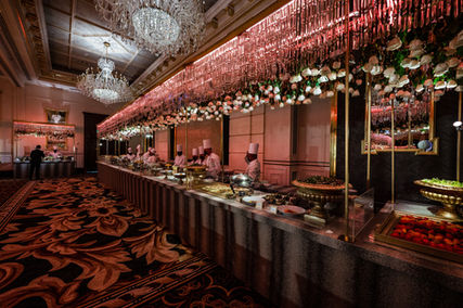 Buffet setup in a ballroom staffed by chefs and decorated with floral garlands