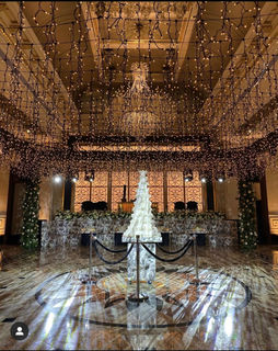 Tall wedding cake displayed under a canopy of fairy lights in an ornate event hall