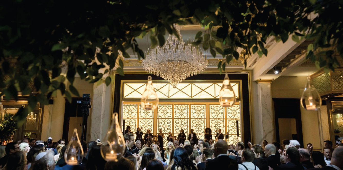 Crowded ballroom reception at Shadowbrook beneath a large chandelier and hanging glass candle holders