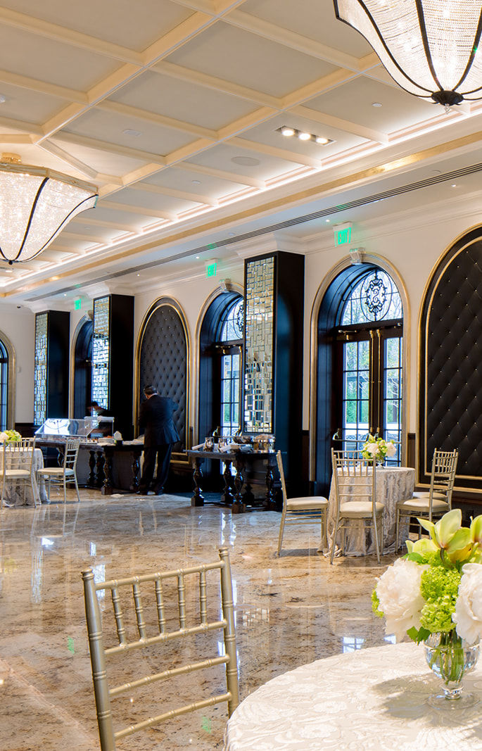 Marble-floored event room with arched windows, coffered ceiling and cocktail tables set for a reception