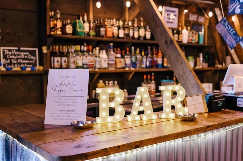 Rustic wooden bar with illuminated BAR marquee letters and a drink menu sign