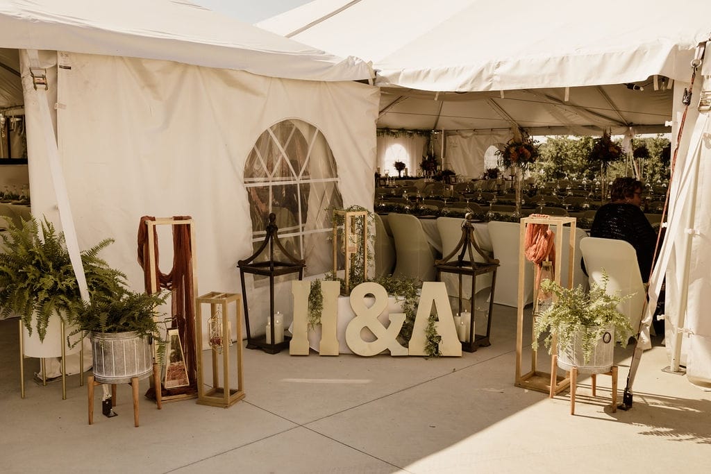 Tent entrance decorated with wooden lanterns, potted ferns, and monogram letters