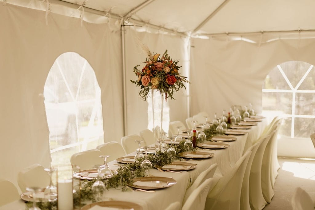 Long banquet table set with floral centerpieces and gold chargers inside the tent