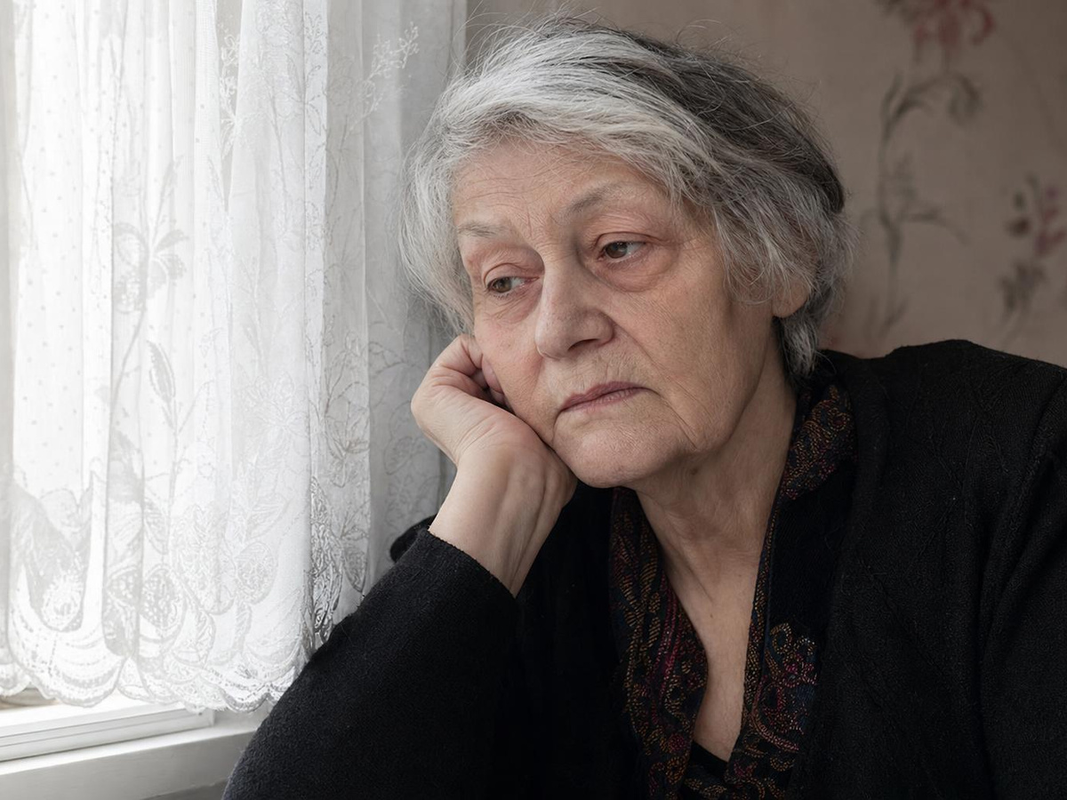 An older woman looking tired and unwell, sitting by a window