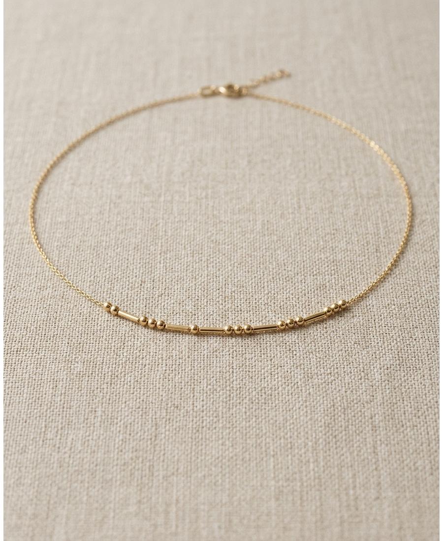 A delicate gold Morse code necklace laid on neutral linen