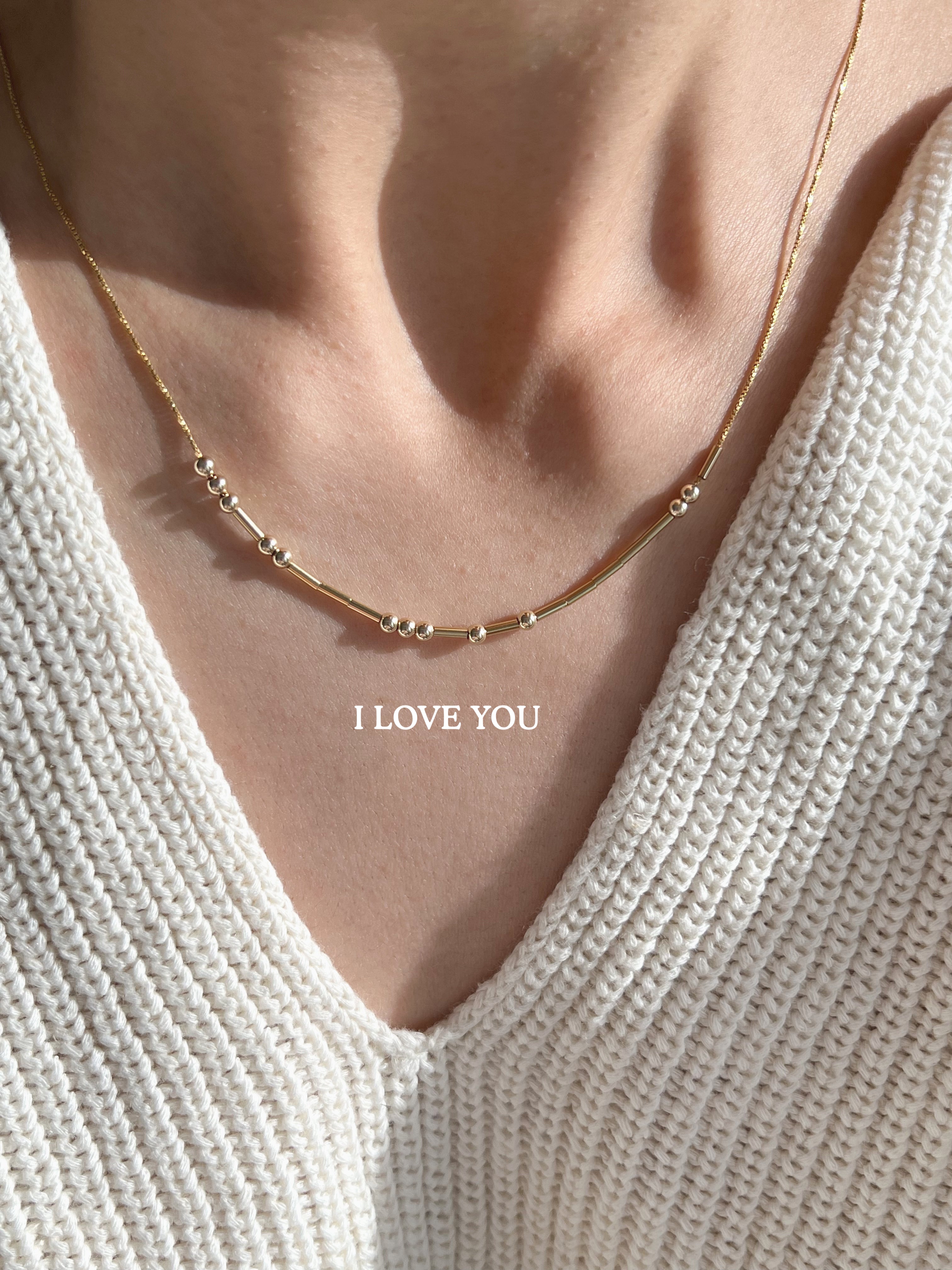 A dainty gold Morse code necklace spelling a hidden message, worn close to the collarbone