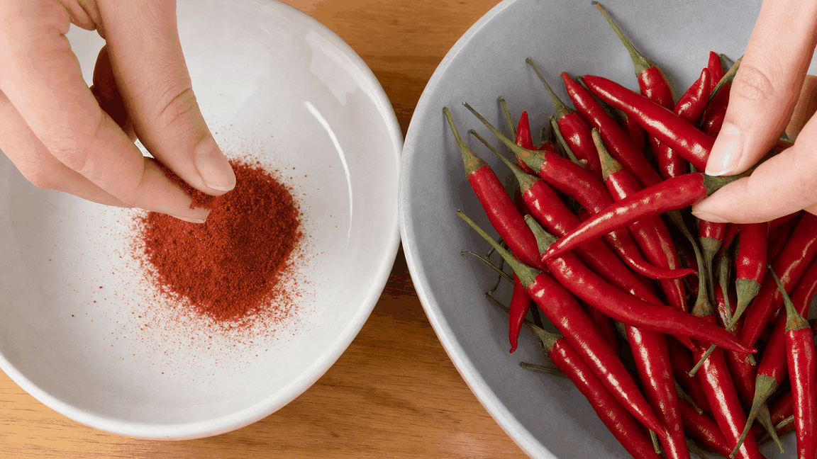 Fresh red cayenne chillies in a bowl beside a bowl of ground cayenne