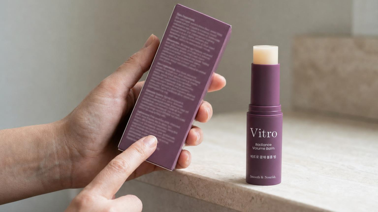 A hand holding a box, fingertip low on a long block of fine ingredient print, beside the Vitro K-Beauty Balm