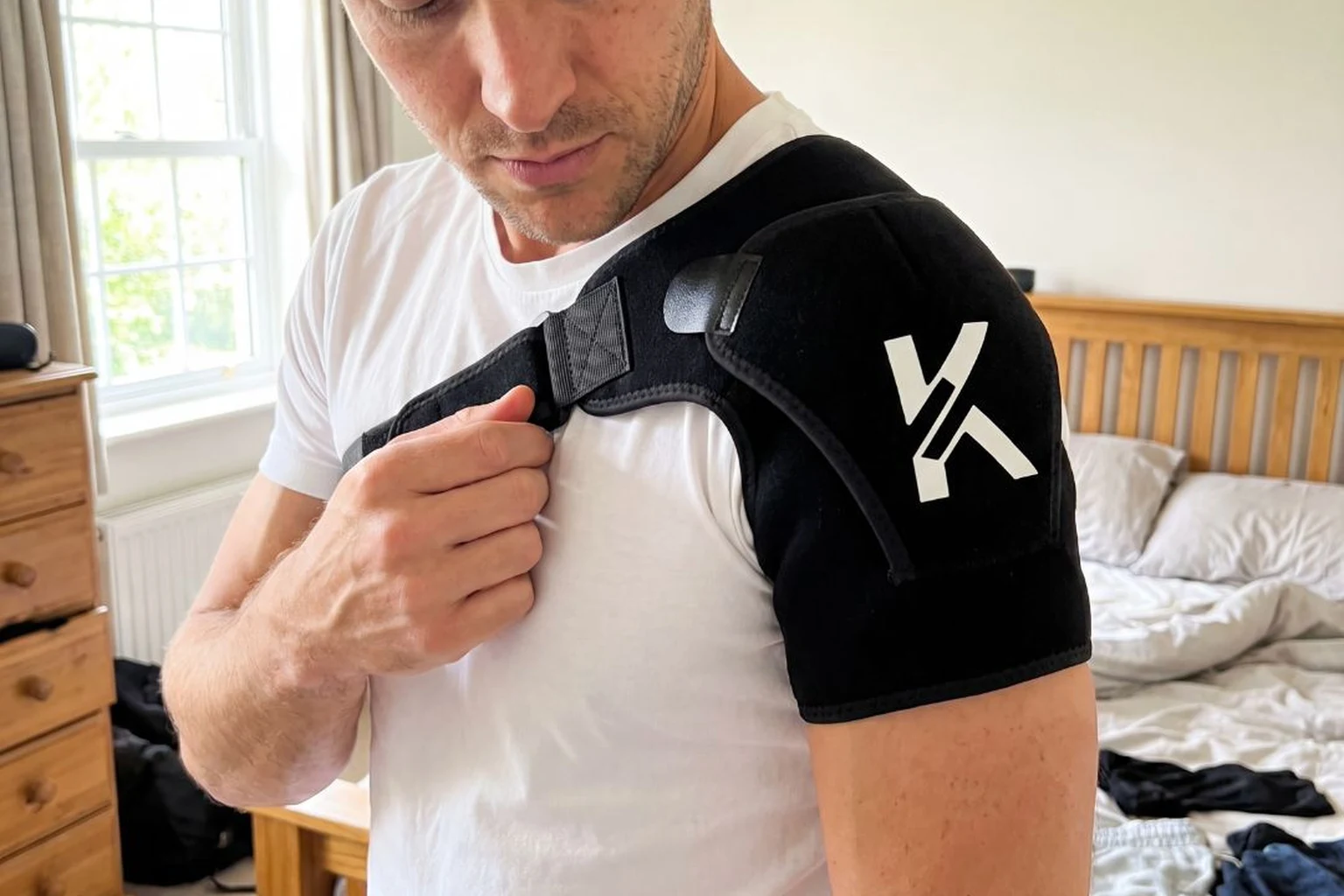 Man fastening a black neoprene shoulder brace across his chest at home
