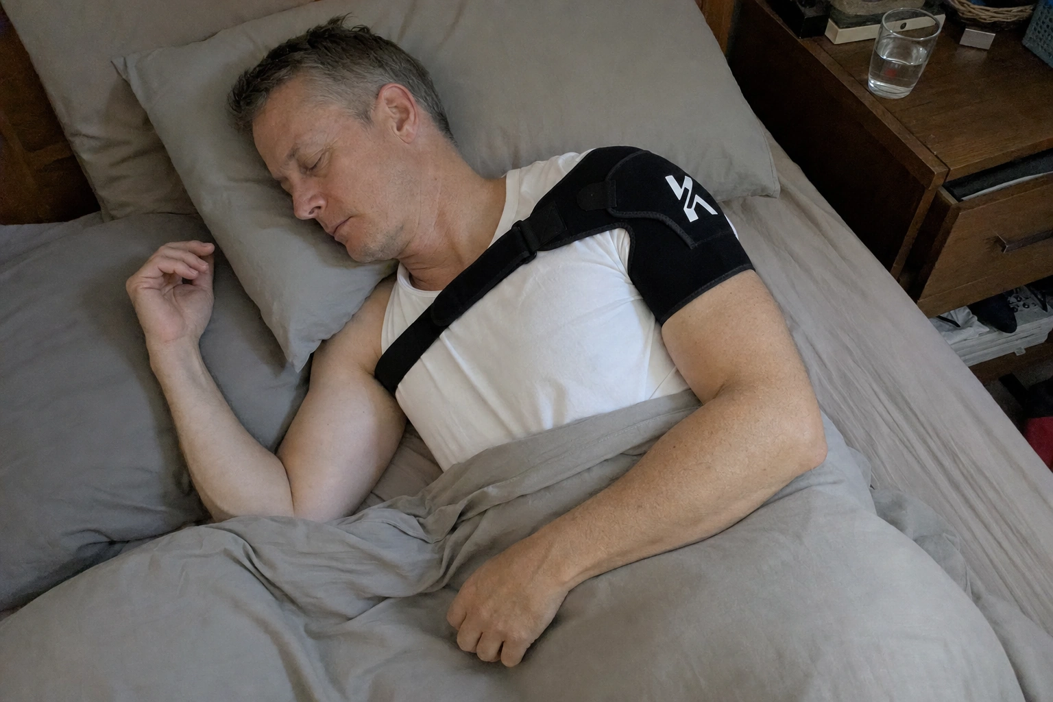 Man asleep on his side at night wearing a black shoulder support brace over his t-shirt