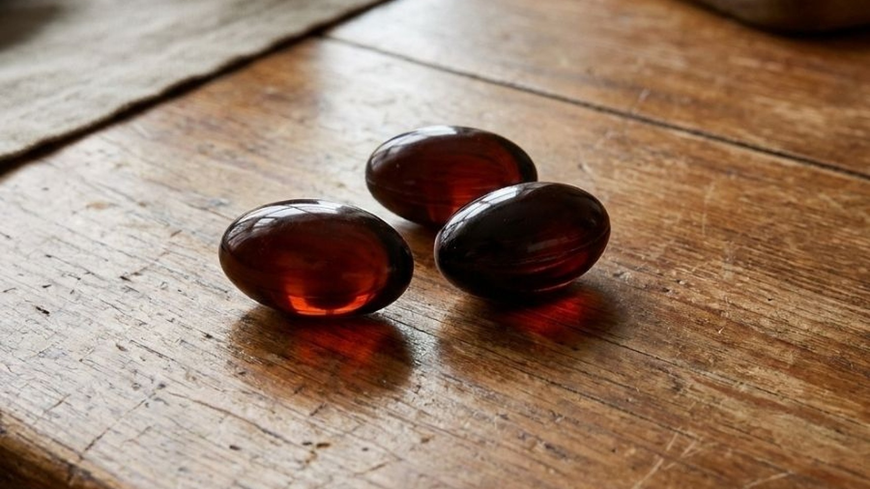 Dark red softgels resting on a wooden kitchen table