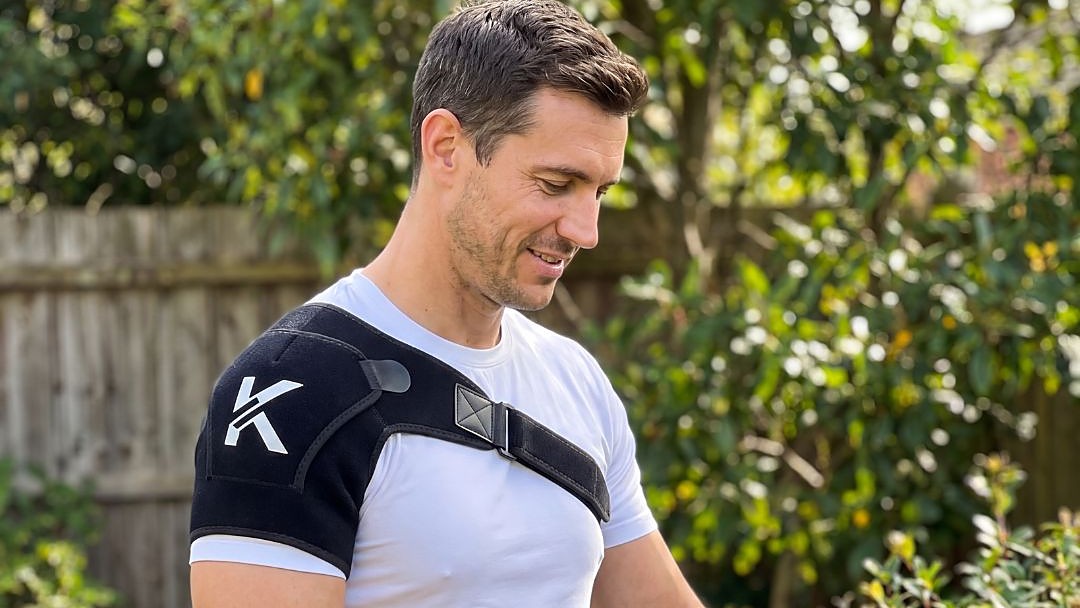 Man wearing the Kinetics brace over a white T-shirt while trimming a hedge