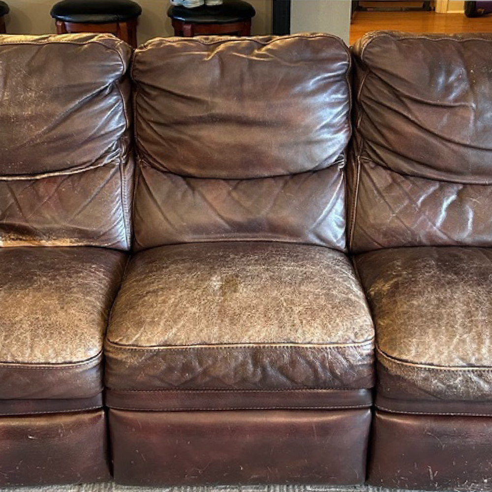 A brown leather sofa faded pale across the seat cushions and arms