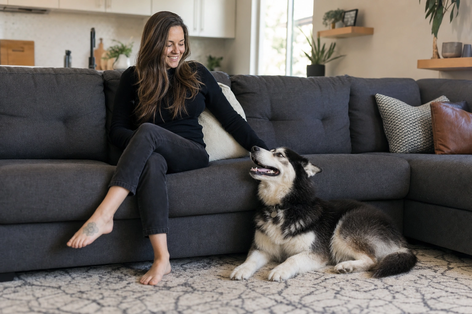 Woman in black jeans sitting on a clean fur-free sofa at home with her husky mix resting beside her