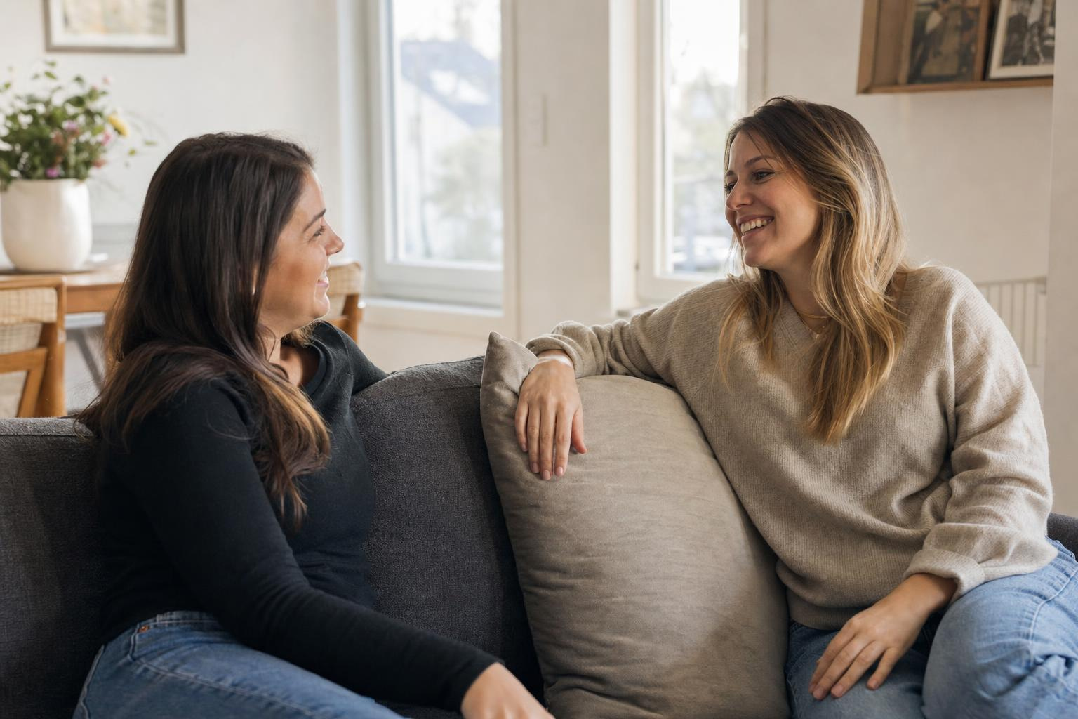 Two friends sitting on a clean sofa talking, one running her hand over the fur-free cushion