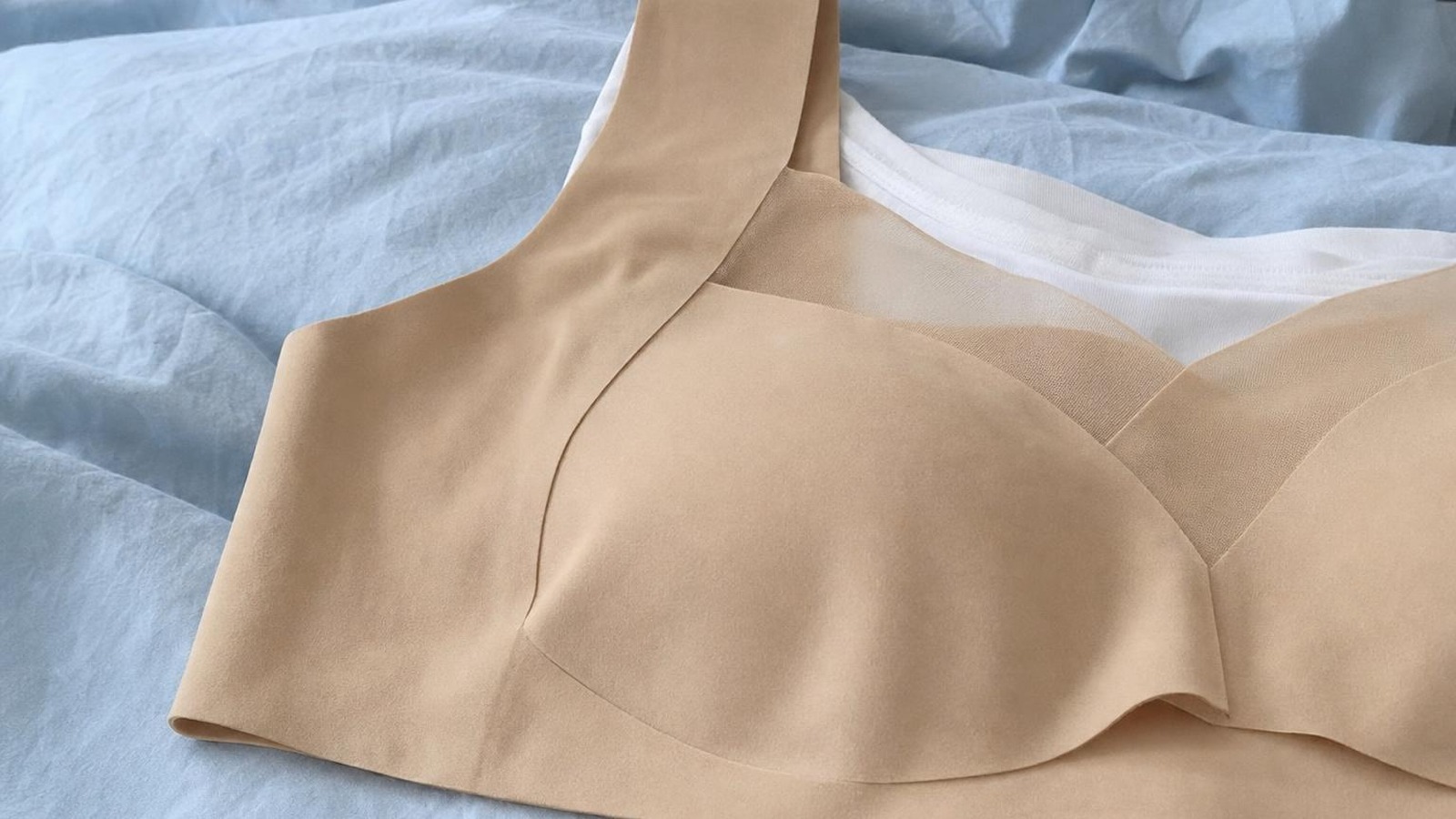 Primo piano del reggiseno beige sul piumone: bordi lisci senza cuciture, bretella larga e inserto in rete trasparente sul davanti