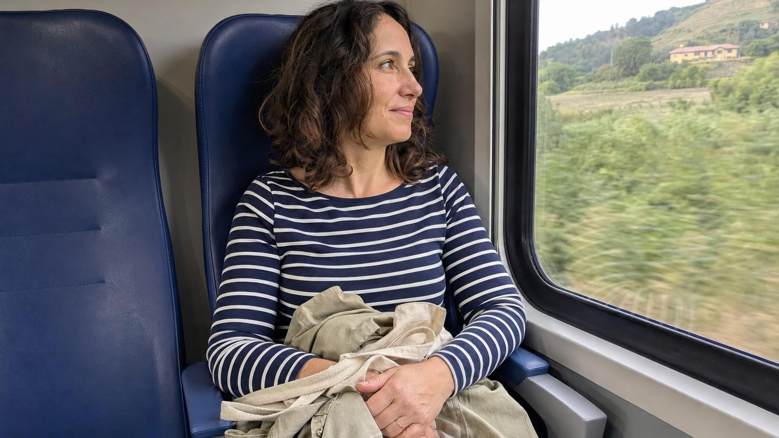 Una donna in treno guarda fuori dal finestrino, vestita con una maglia aderente