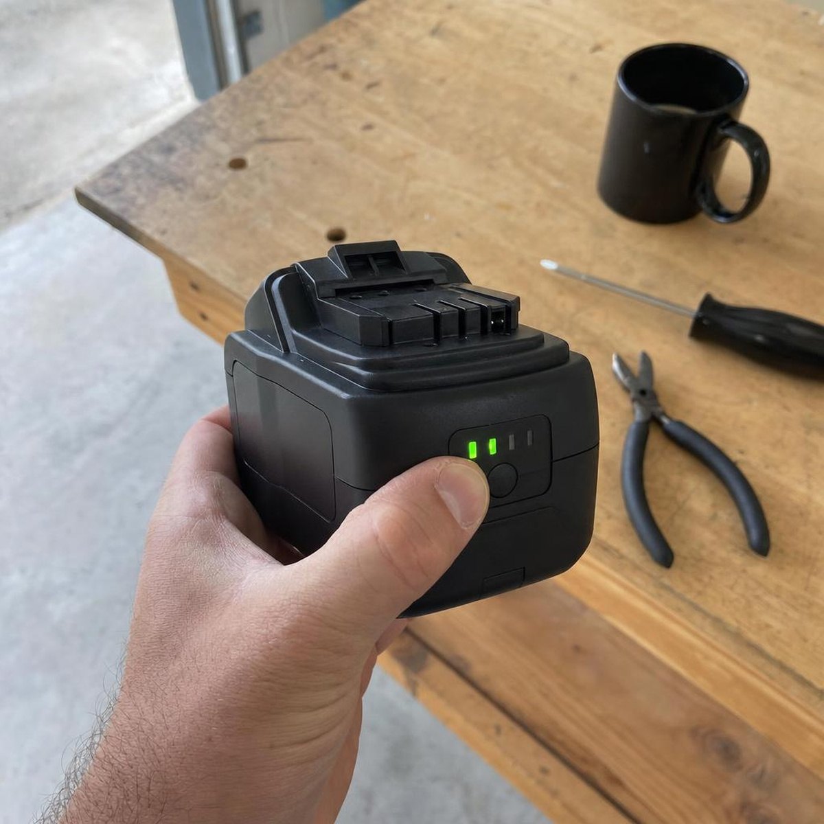 A hand pressing the fuel gauge on a cordless tool battery that still shows charge