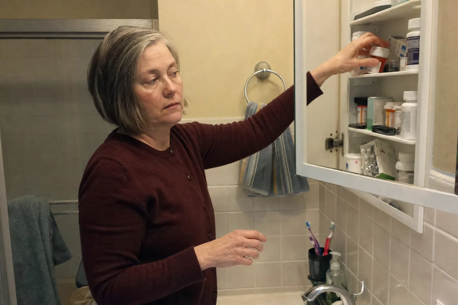 Woman reaching into a bathroom cabinet crowded with pill bottles