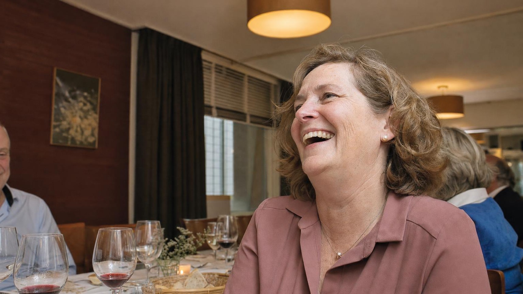 A woman in her fifties laughing at a family dinner, photographed from slightly below