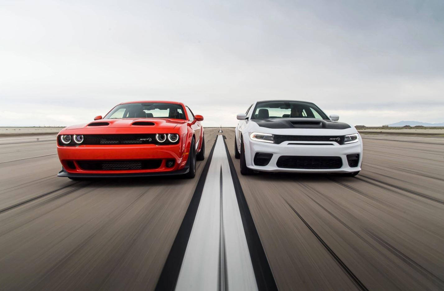 a red-orange Dodge Challenger races a white Dodge Charger with a black hood