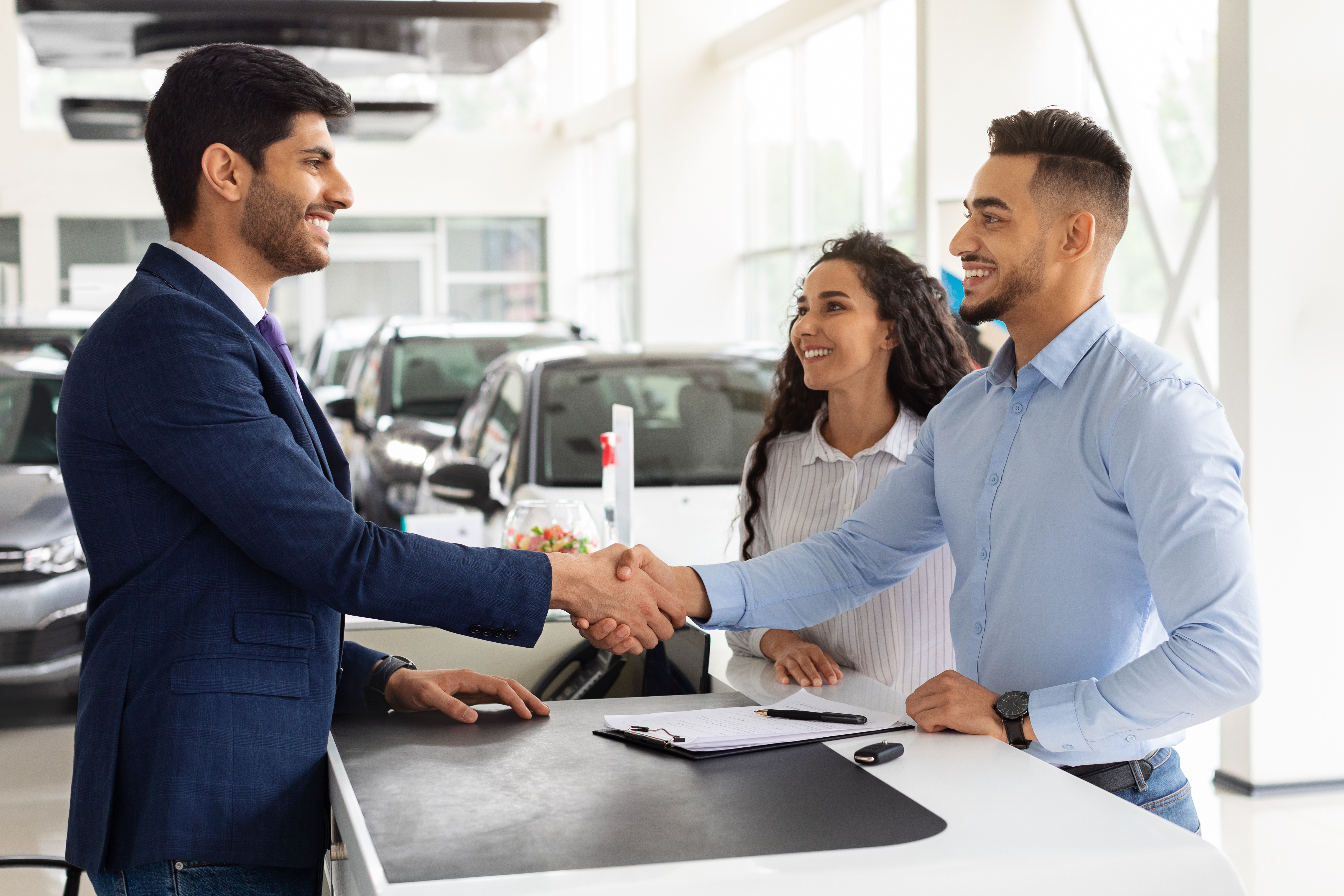 a smiling couple shaking hands with the car salesman inside of a dealership