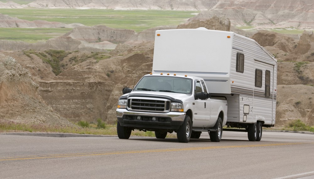 white pickup truck towing a camper up a steep hill with mountains in the background