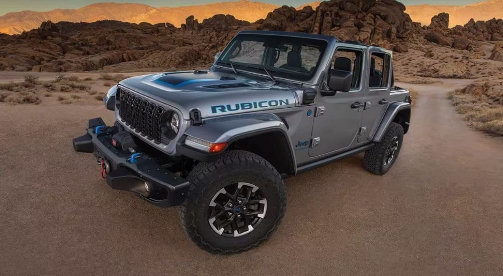 A grey 2024 Jeep Wrangler Rubicon is shown from the side while crawling over rocks.