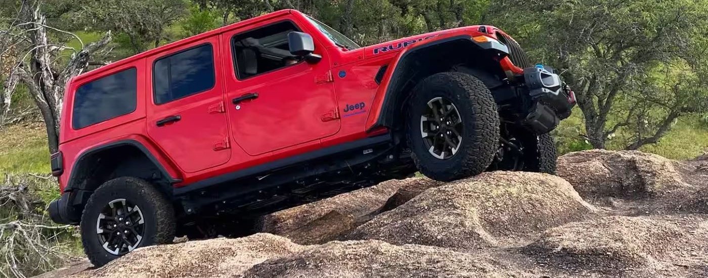 A red 2024 Jeep Wrangler Rubicon 4xe is shown from the side while off-road after leaving a Jeep dealer near DeKalb.