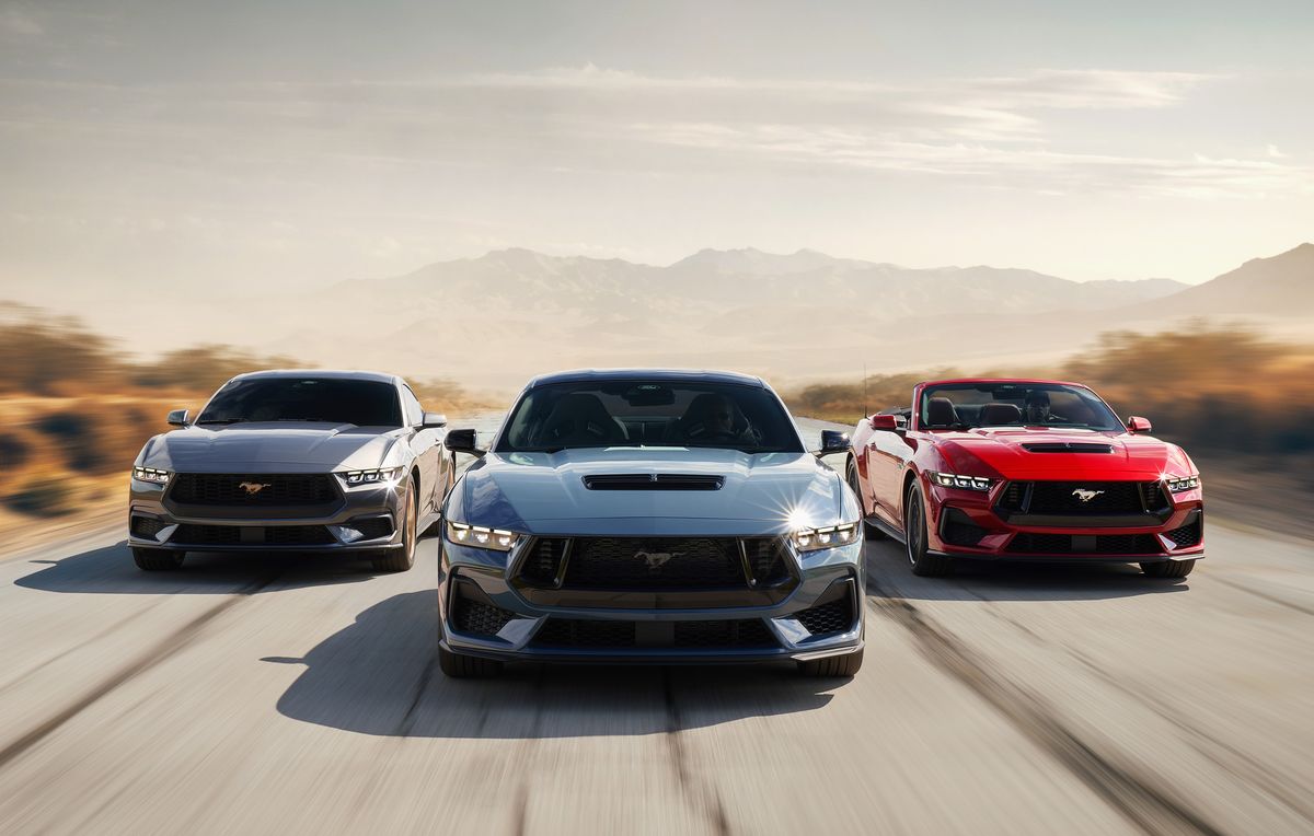 Pictured left to right: Gray 2024 Ford Mustang, blue 2024 Ford Mustang, red 2024 Ford Mustang driving down a road in the middle of a desert