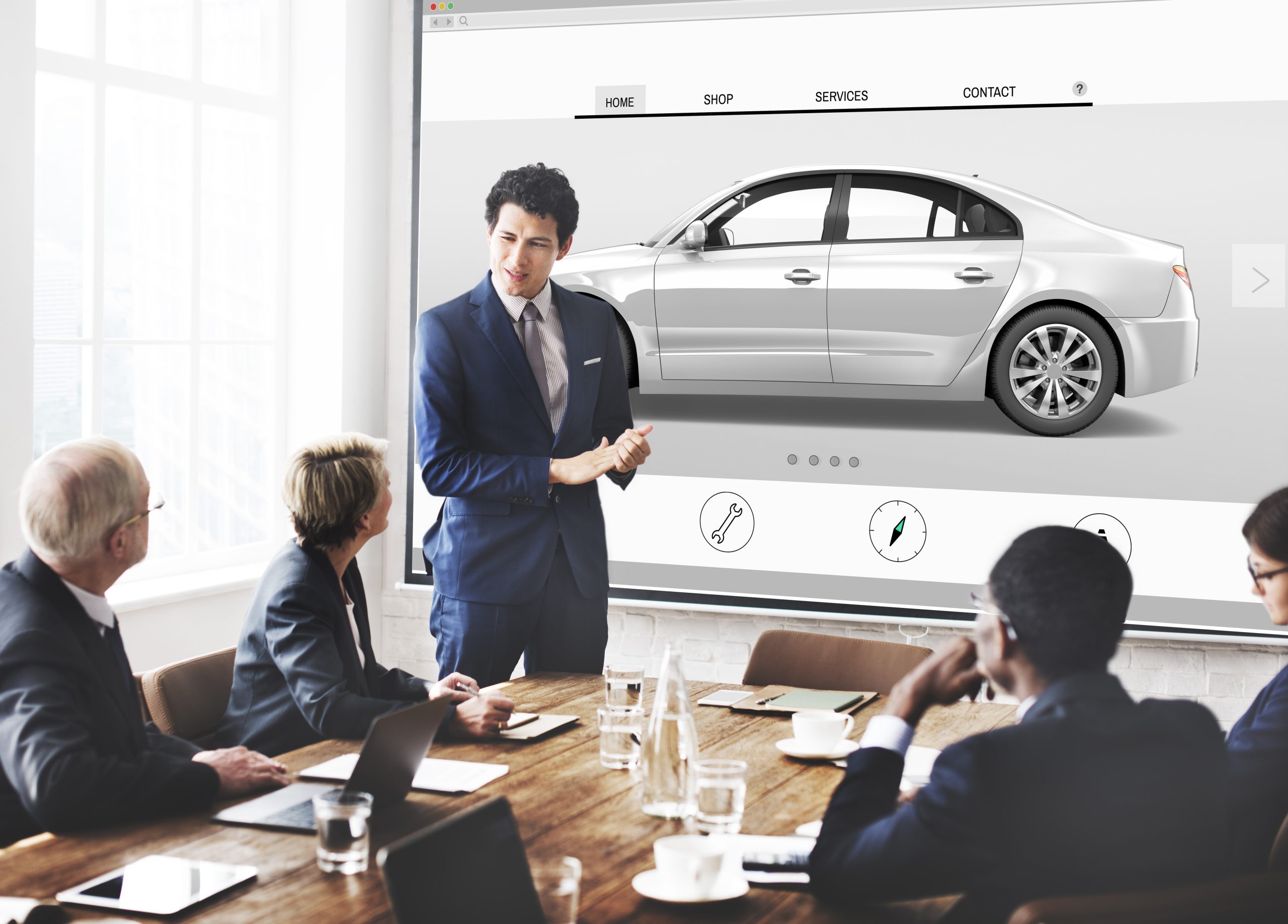 business men in suits in a meeting as one is presenting a silver car on the screen