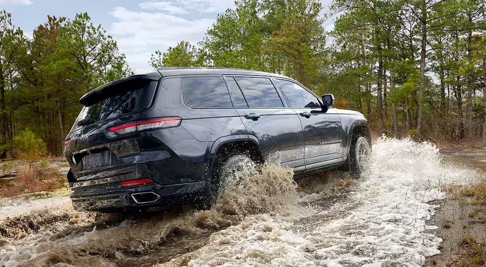 A blue 2024 Jeep Grand Cherokee is off-roading through a river.