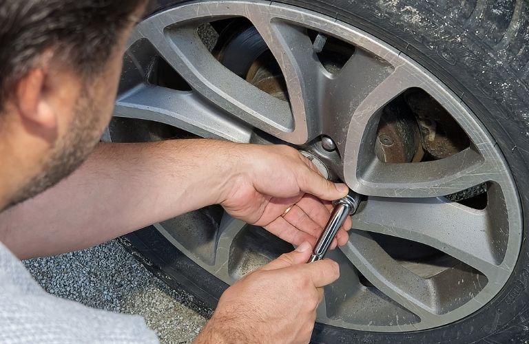 A person using a lug wrench to loosen/tighten the nuts on a wheel