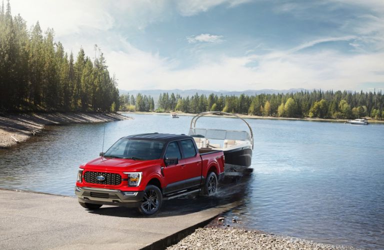 Red 2023 Ford F-150 Heritage Edition Towing a Boat at a Landing