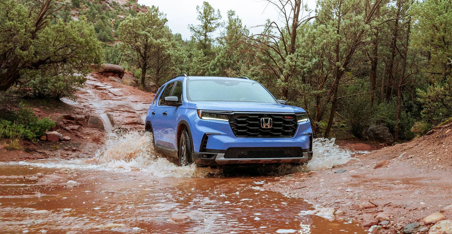 blue 2025 Honda Pilot TrailSport off-roading through a creek