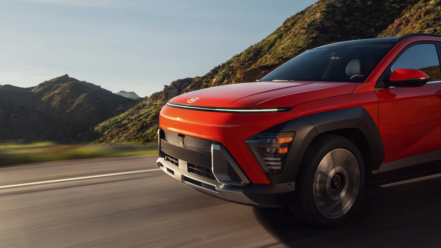 A red Hyundai Kona driving on a dirt road.