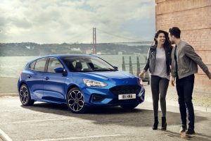 a couple standing next to a blue 2019 Ford Focus with the Golden Gate Bridge in the background