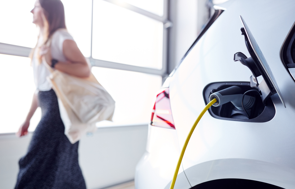 woman walks past an electric vehicle while it charges in a garage
