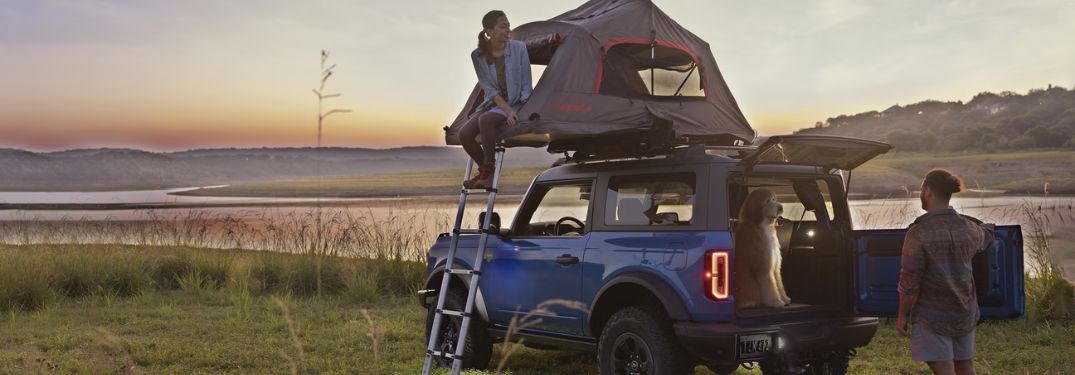 Blue 2024 Ford Bronco with Roof Mounted Tent and Couple by Lake at Sunset