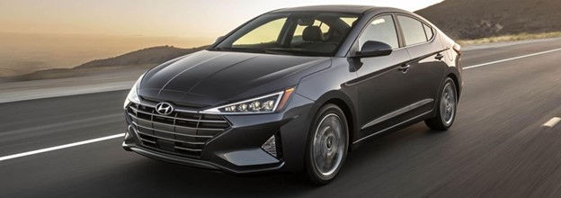 a gray sedan driving on a highway next to water