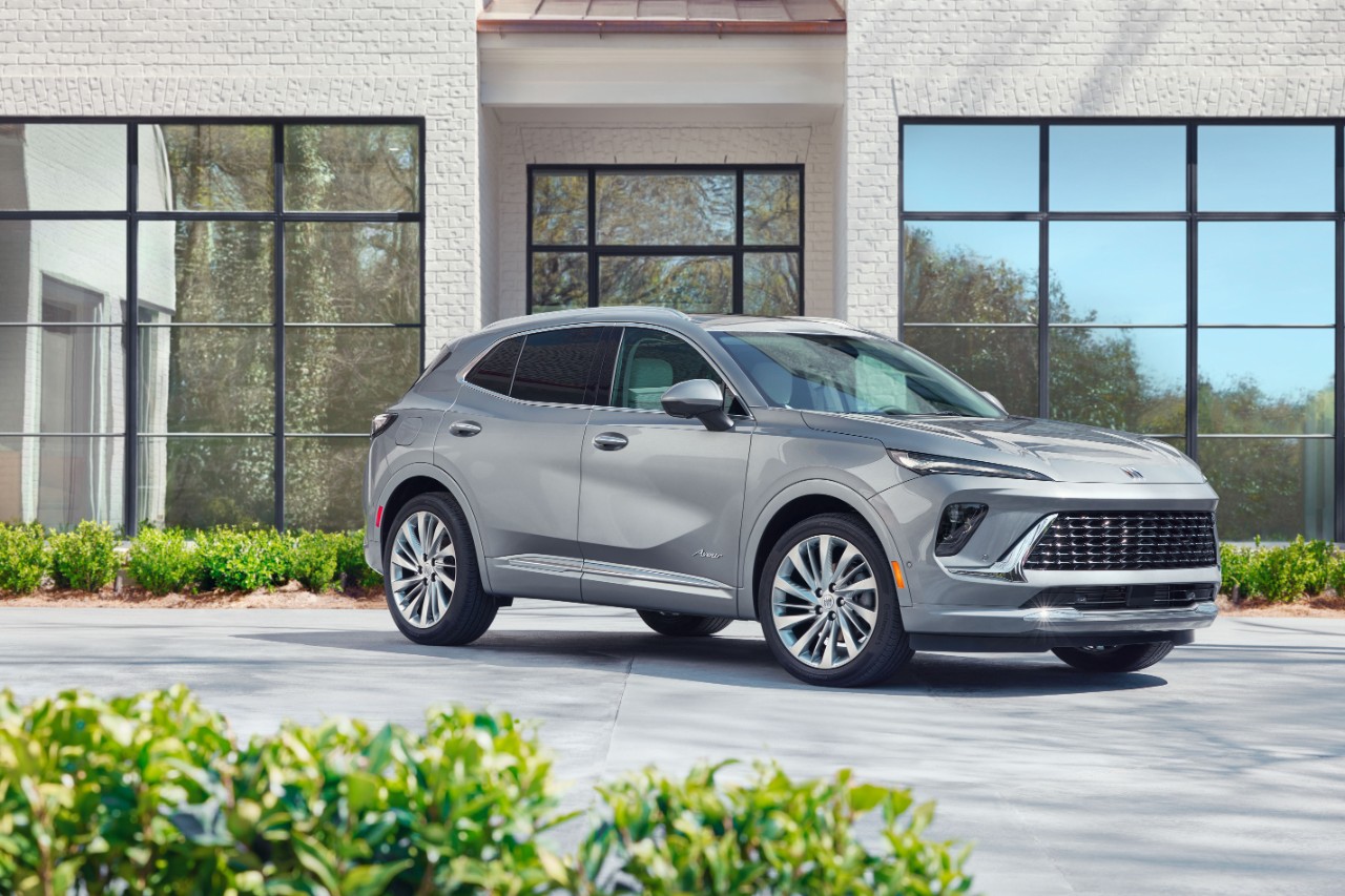 Front 3/4 view of the 2024 Buick Envision Avenir in Moonstone Gray Metallic in front of white building. 