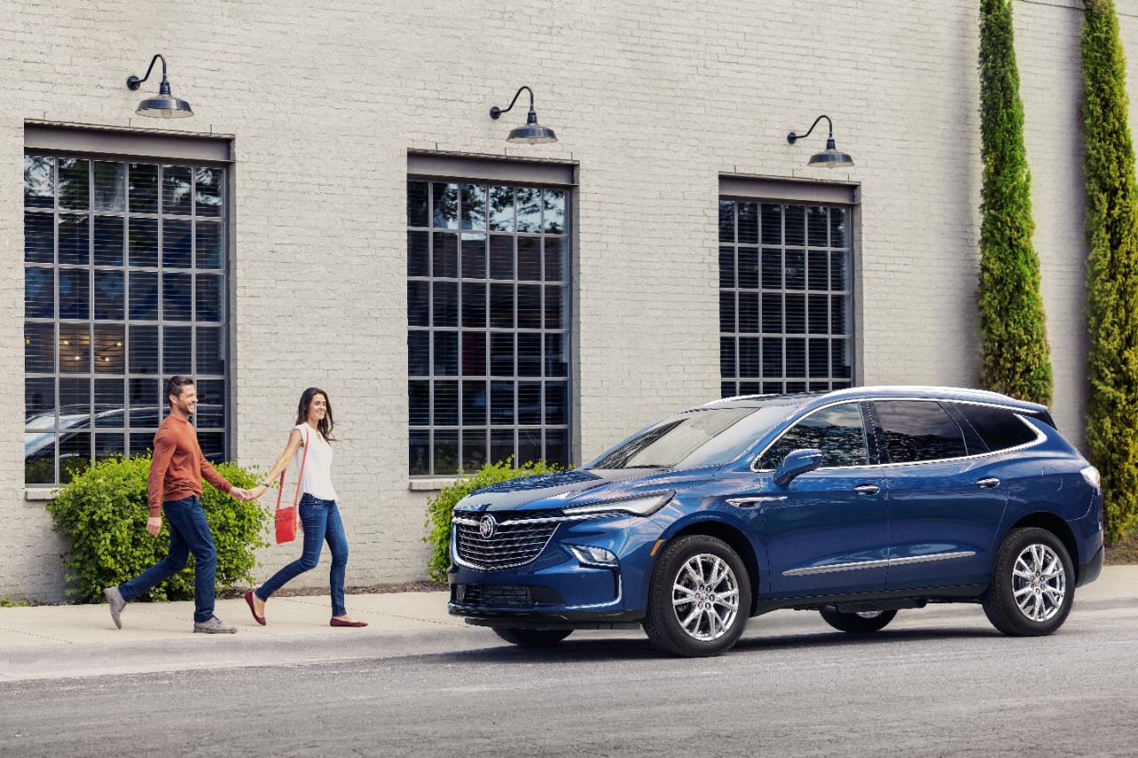 A front 3/4 view of the 2024 Buick Enclave Premium in Emperor Blue Metallic with a couple walking toward it.
