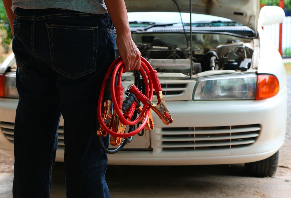 Man holding jumper cables, facing his vehicle's engine