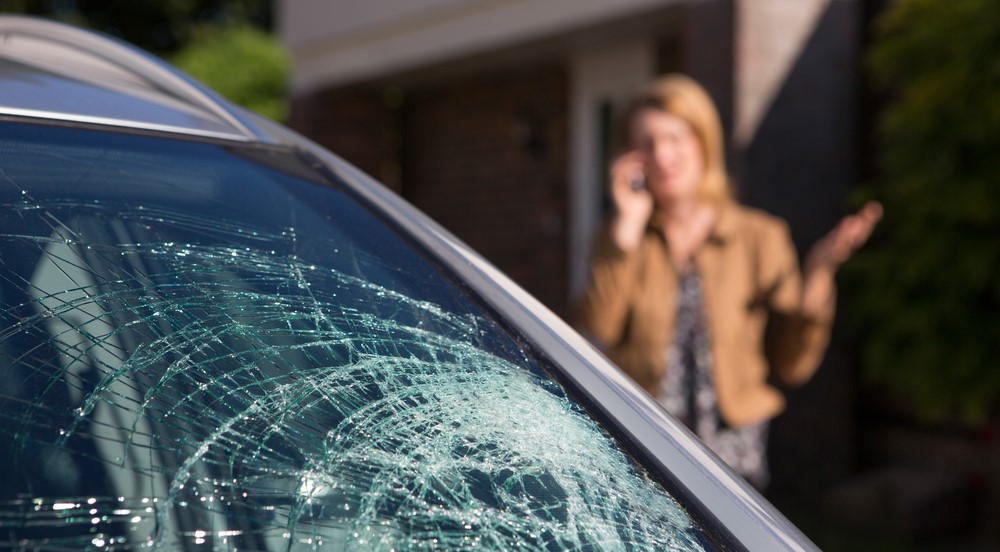 focus on cracked windshield, woman in the background on the phone, looking concerned