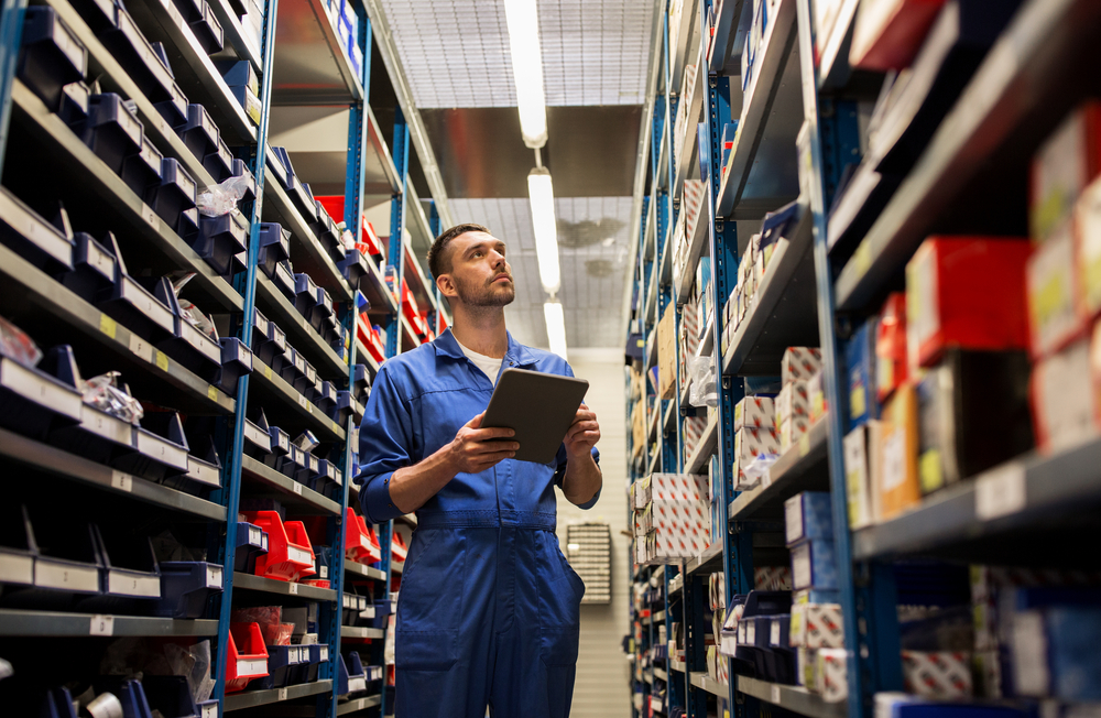 service employee holding clipboard looking for parts in an aisle