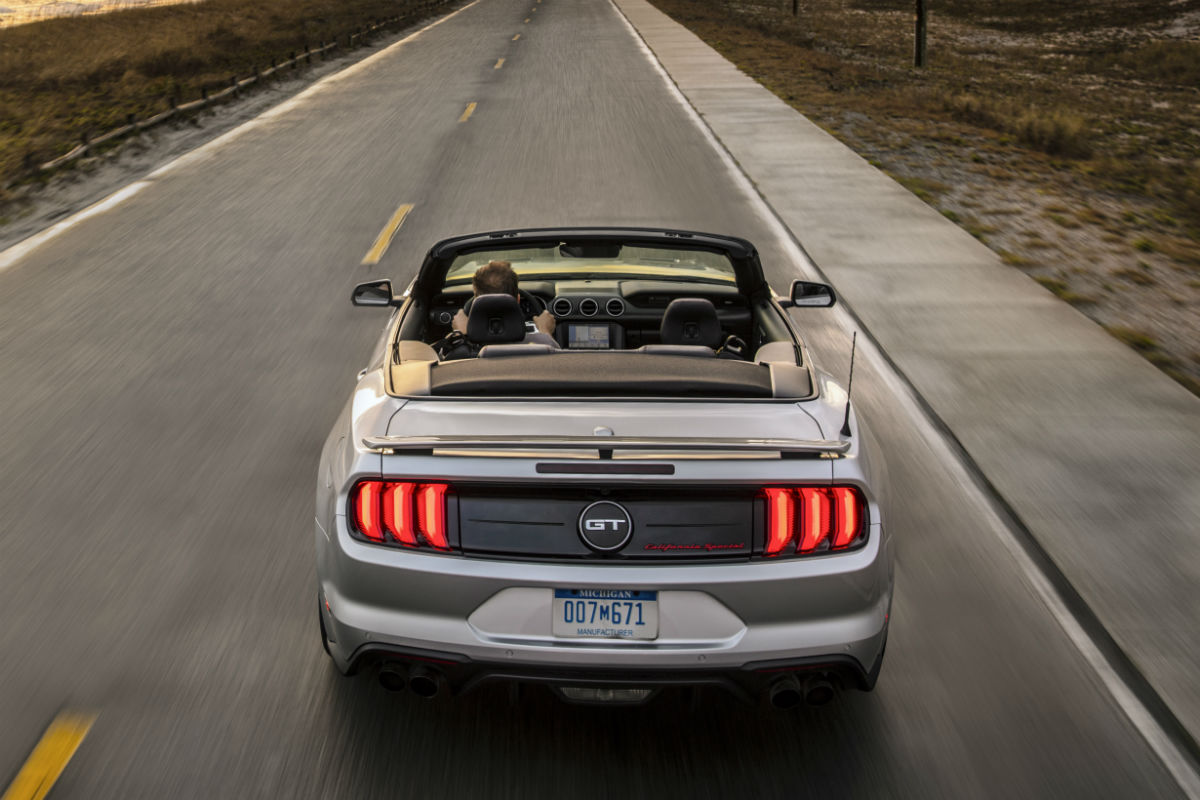 rear view of a silver 2019 Ford Mustang driving along a coastal highway
